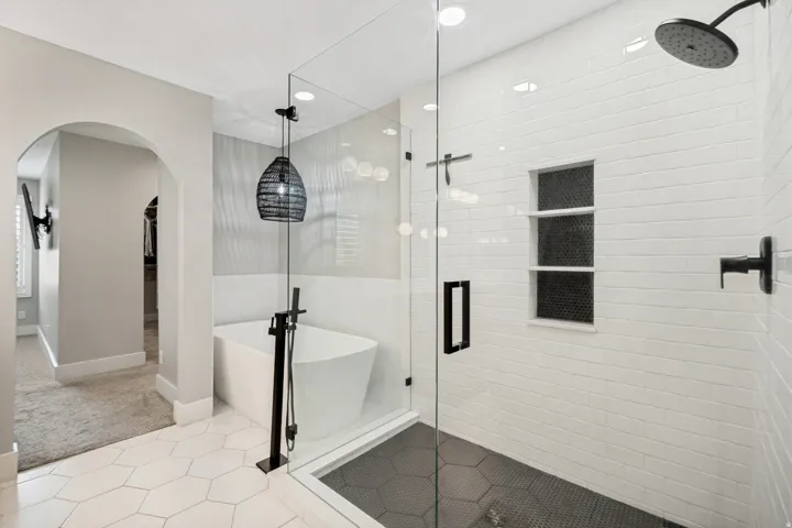 Freestanding bathtub with floor-mounted fixture, glass-enclosed shower with subway tile, built-in shower niche, hexagon floor tiling, and recessed lighting