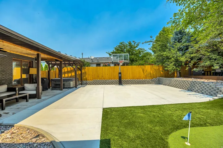 Expansive concrete patio with a basketball hoop, covered outdoor living area, and a putting green