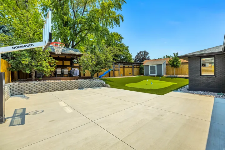 Expansive concrete patio with a basketball hoop, retaining wall, and a raised wooden deck with a gazebo