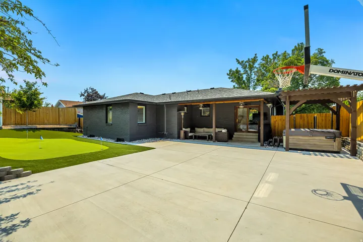 Expansive concrete patio with a built-in putting green, covered outdoor living area, and a hot tub under a wood pergola