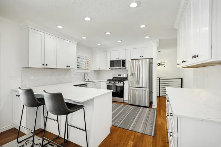 White shaker cabinetry, recessed lighting, stainless steel appliances, solid surface countertops, and wood-finish flooring