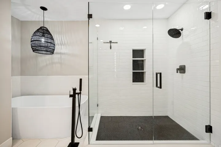 Freestanding soaking tub with floor-mounted fixture, glass-enclosed shower, rain shower head, matte black hardware, and subway tile surround