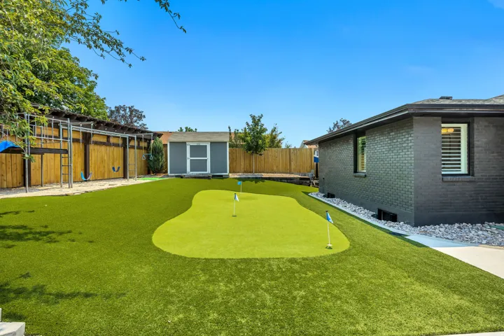 Expansive backyard featuring a putting green, artificial turf, wood fencing, and a detached shed