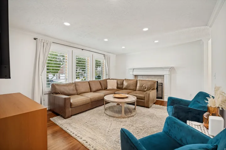 Recessed lighting throughout, wood-finish flooring, white plantation shutters, and a fireplace with a white mantel and tile surround