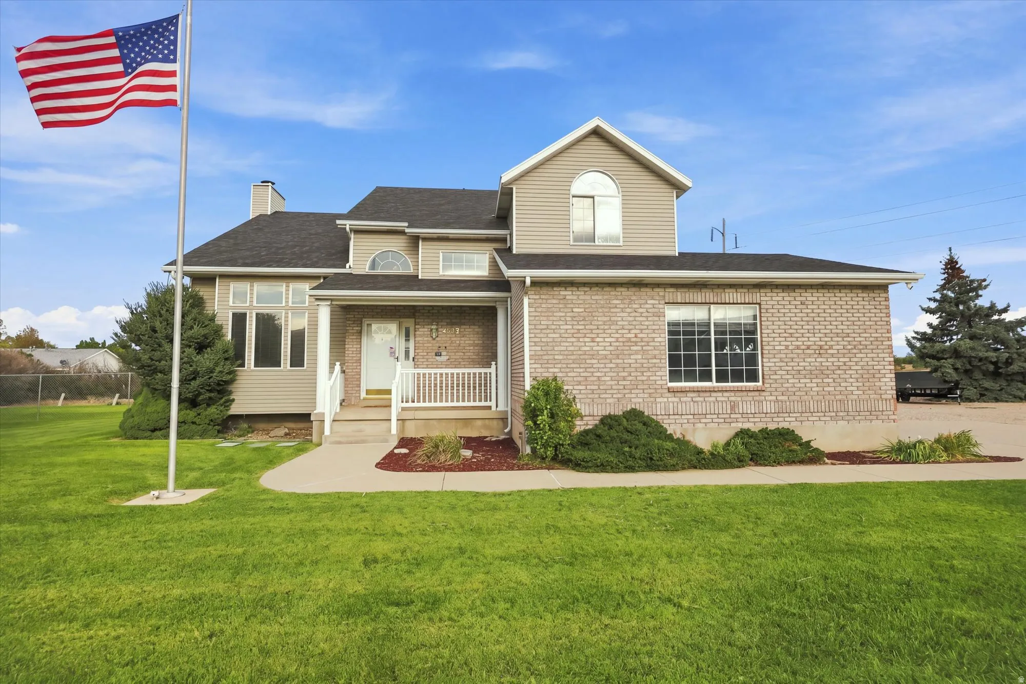 Brick facade with siding accents, covered front porch, large front windows, and landscaped shrubbery