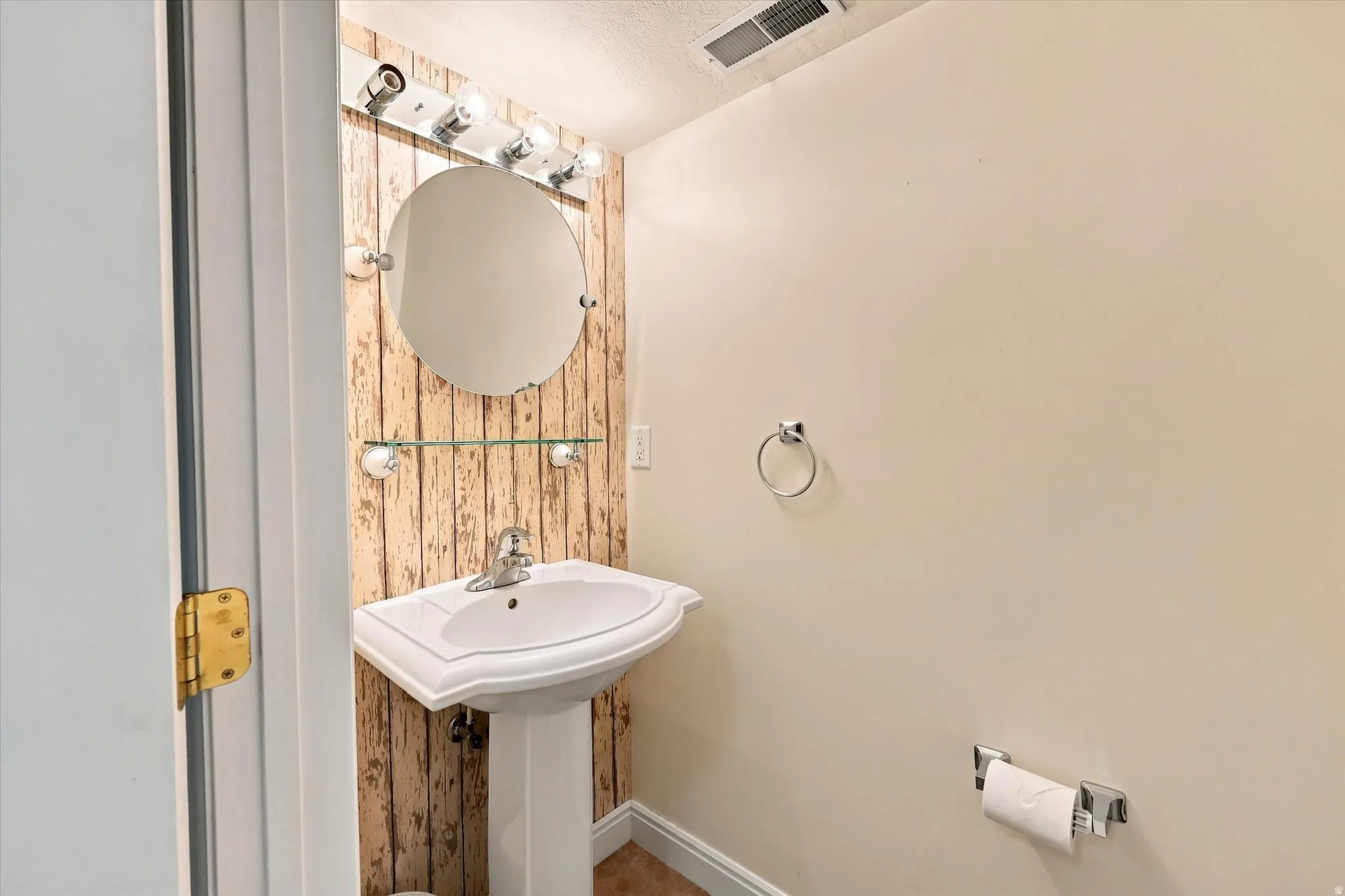 Pedestal sink with chrome faucet, circular mirror, and wall-mounted vanity lighting