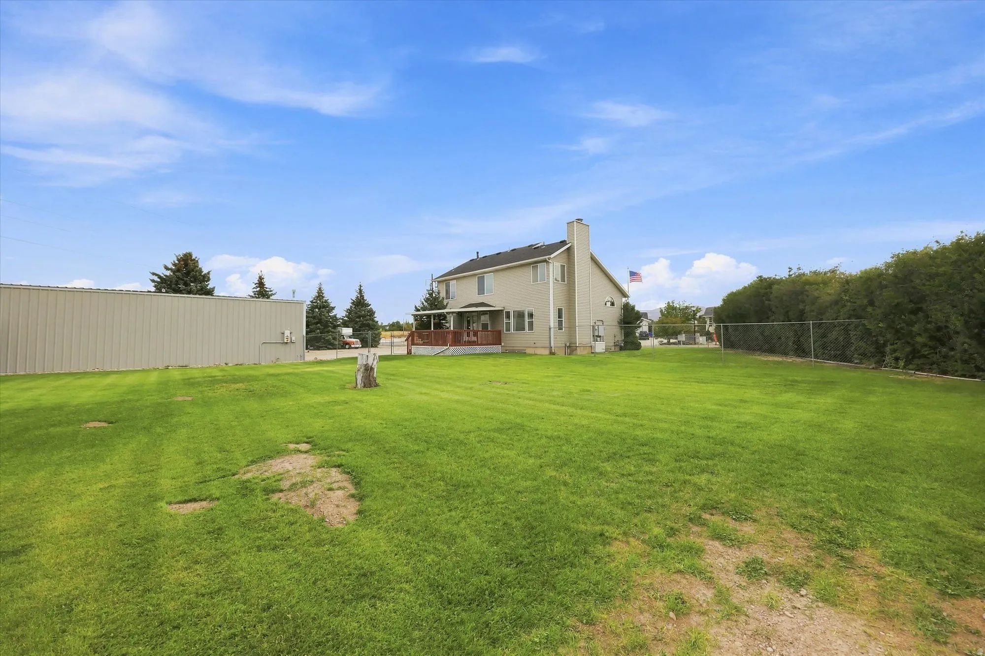 Expansive grassy lawn with a light-colored exterior dwelling, a detached metal-sided structure, and a wood deck