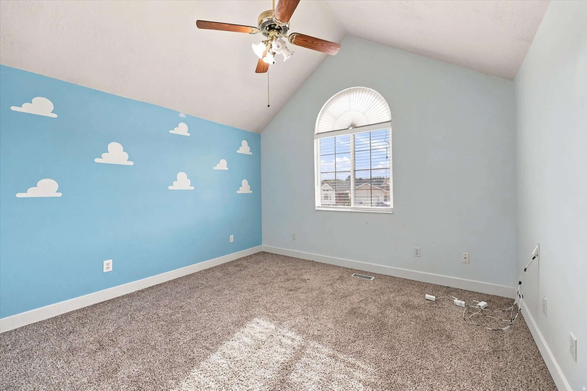 Vaulted ceiling with an attached ceiling fan, arched window with horizontal blinds, cloud-patterned accent wall, and carpeting