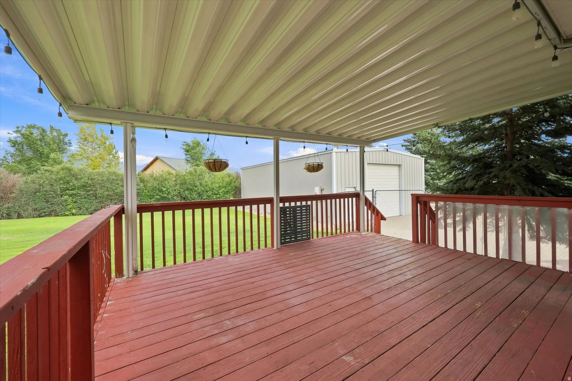 Expansive covered deck with red-stained wood flooring and railing, offering an outdoor living space
