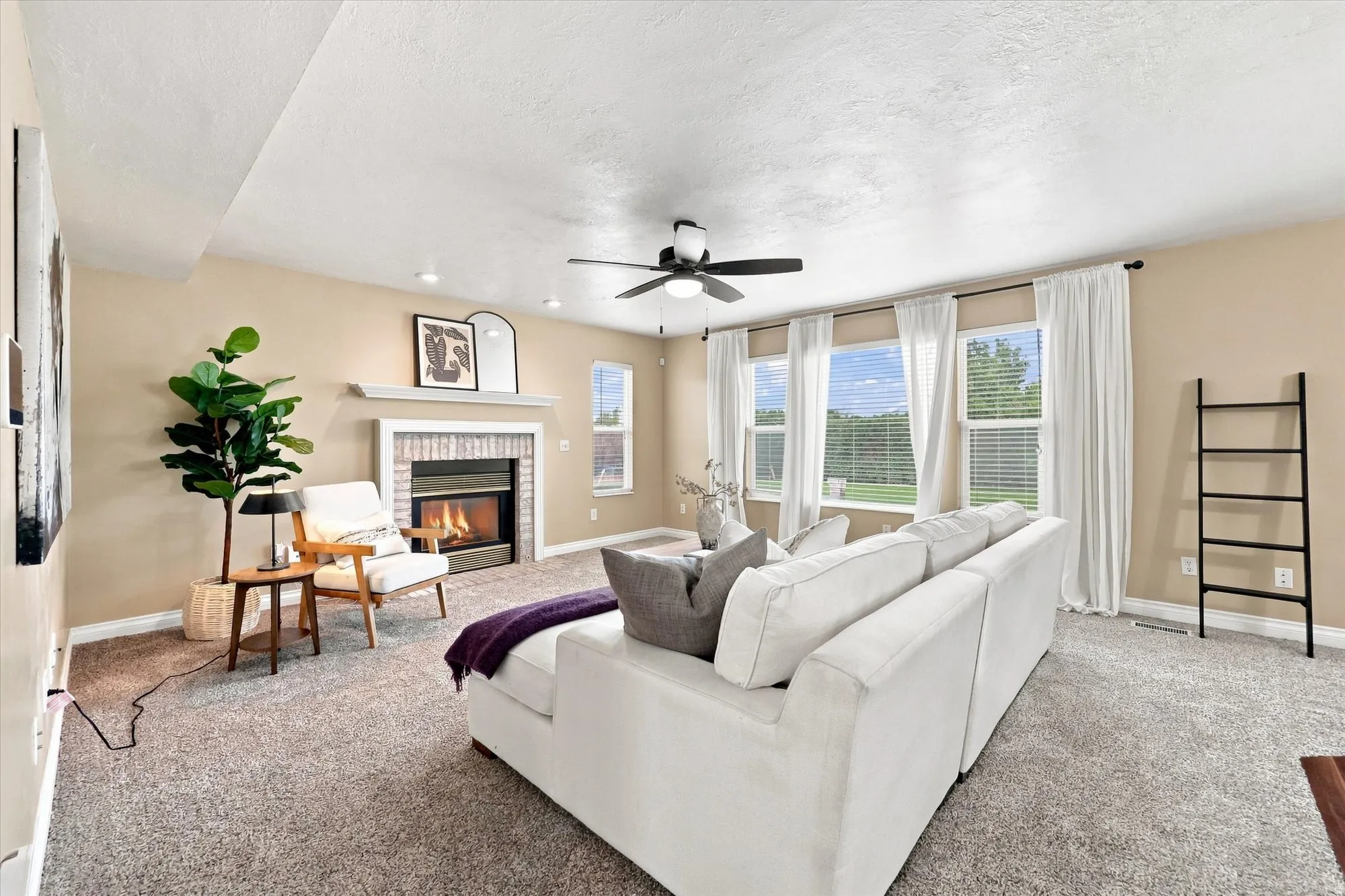 Open-concept living space featuring a fireplace with brick surround, ceiling fan, recessed lighting, and multiple windows