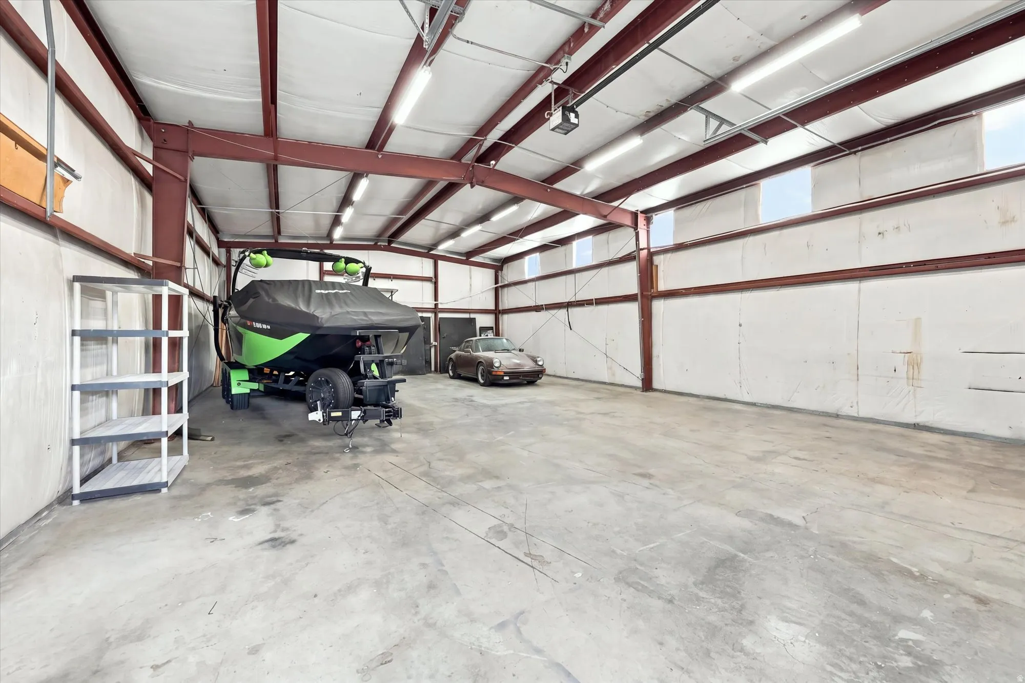 Expansive garage space featuring a concrete floor, exposed structural beams, ceiling-mounted lighting, and transom-style windows