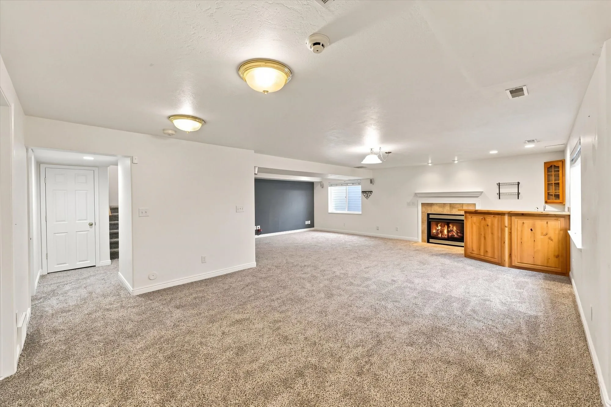 Expansive carpeted area featuring a built-in wet bar, a fireplace with a tile surround and mantel, and recessed lighting