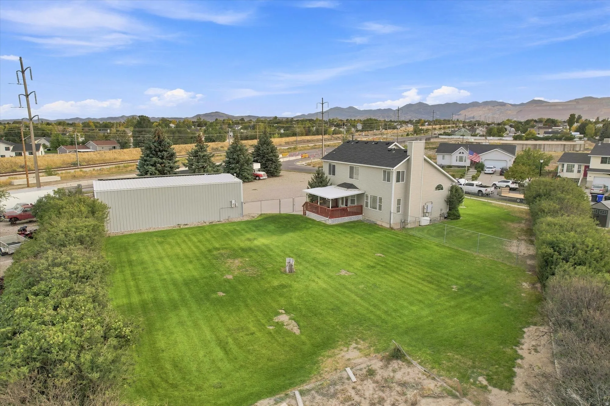 Expansive green lawn with a large detached metal structure and a two-story residence featuring an outdoor deck