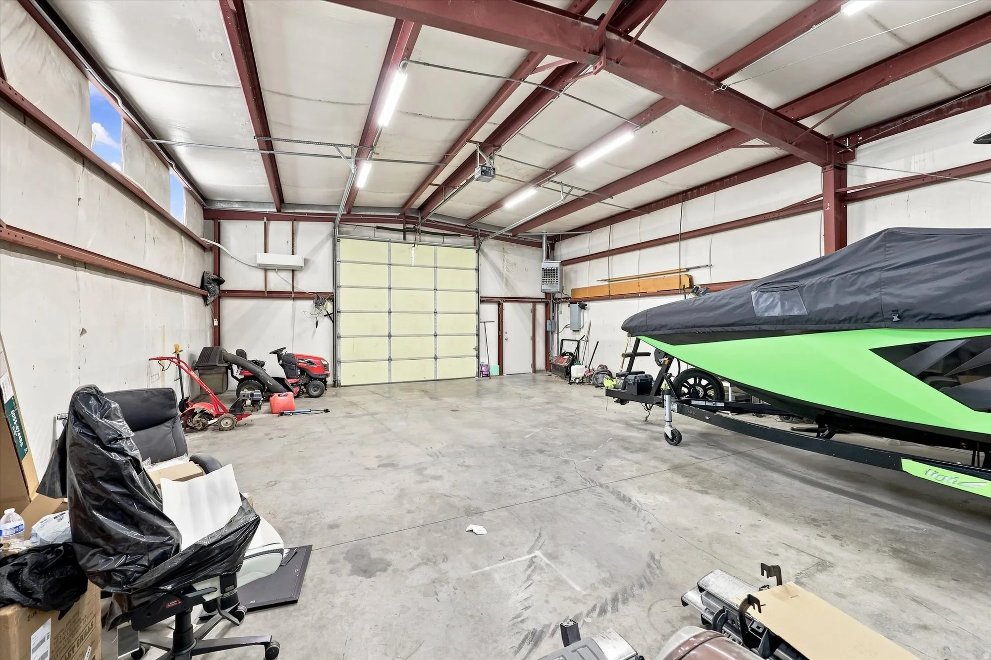 Spacious garage featuring a large overhead door, concrete flooring, exposed beam ceiling, and fluorescent lighting