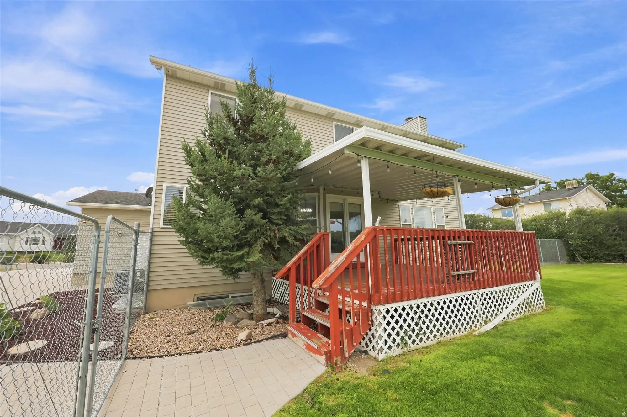 Rear exterior featuring a covered deck with red railings, light beige siding, and a chain-link fenced area