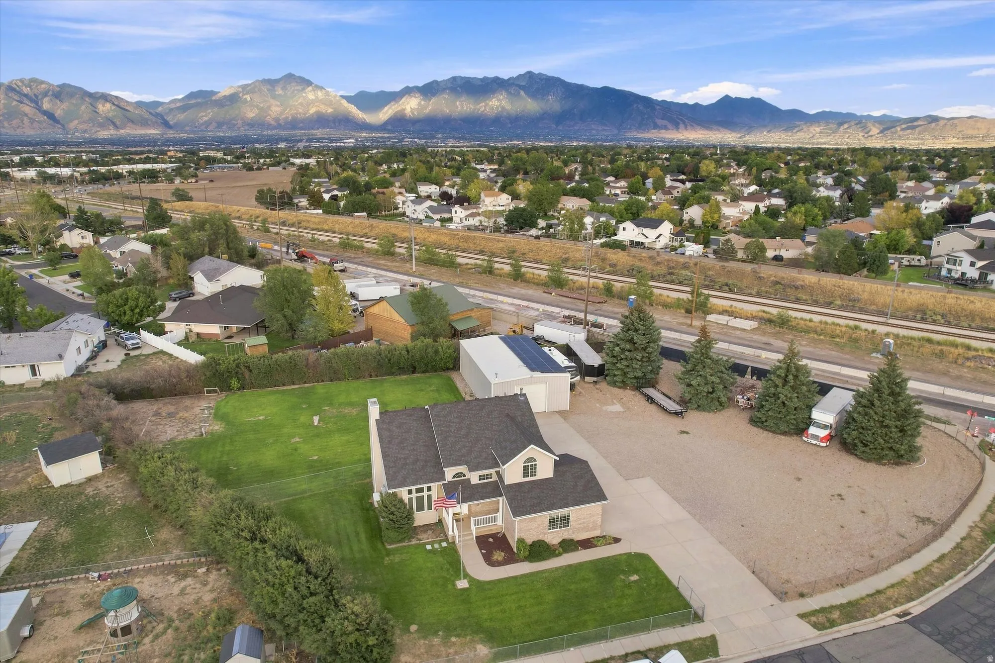 Expansive lot featuring a substantial gravel parking area, mature evergreen trees, and a two-story residence with a gabled roof