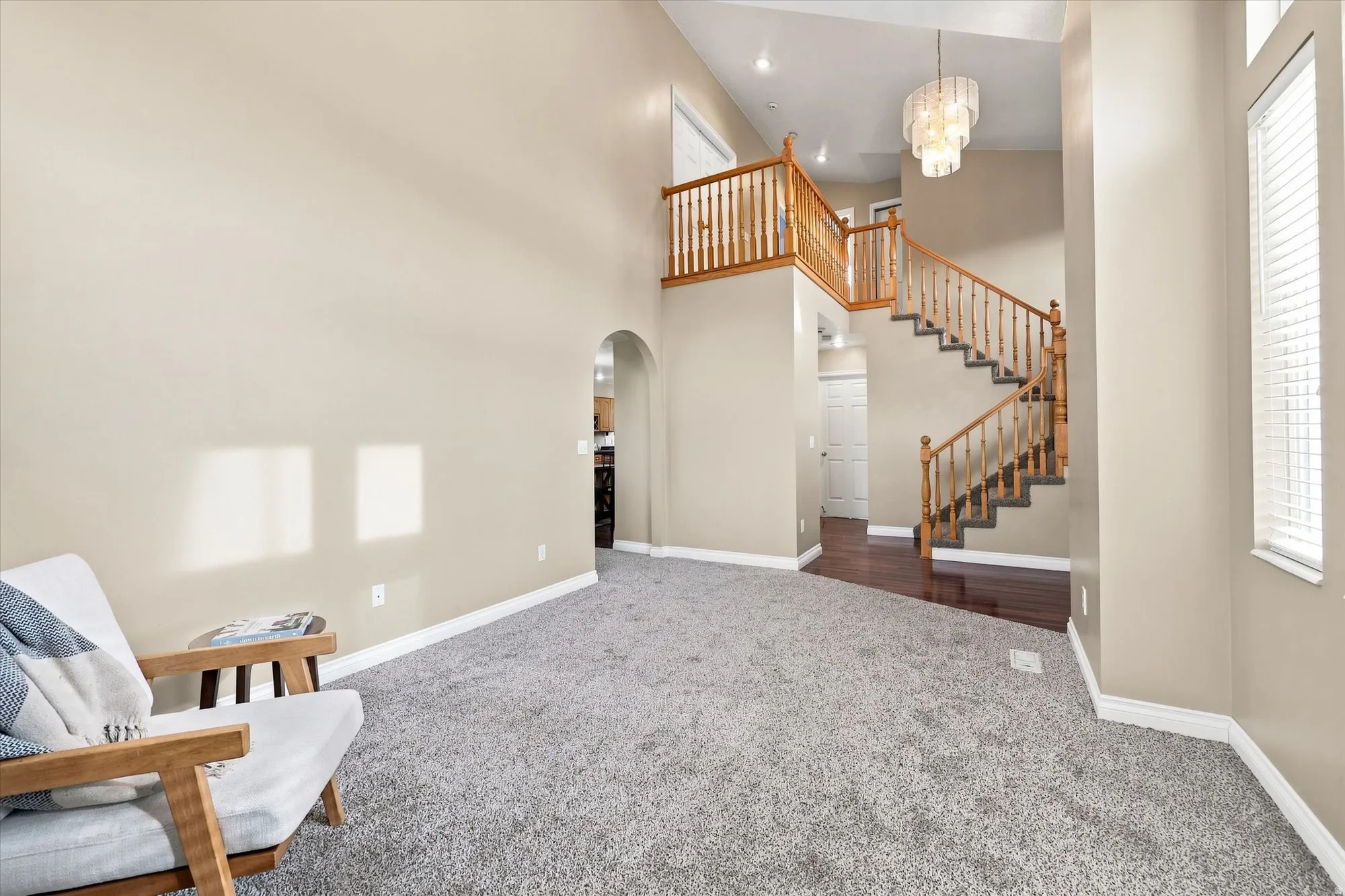 Vaulted ceilings, wood-finish staircase with balusters, upper landing, contemporary chandelier, and arched doorway