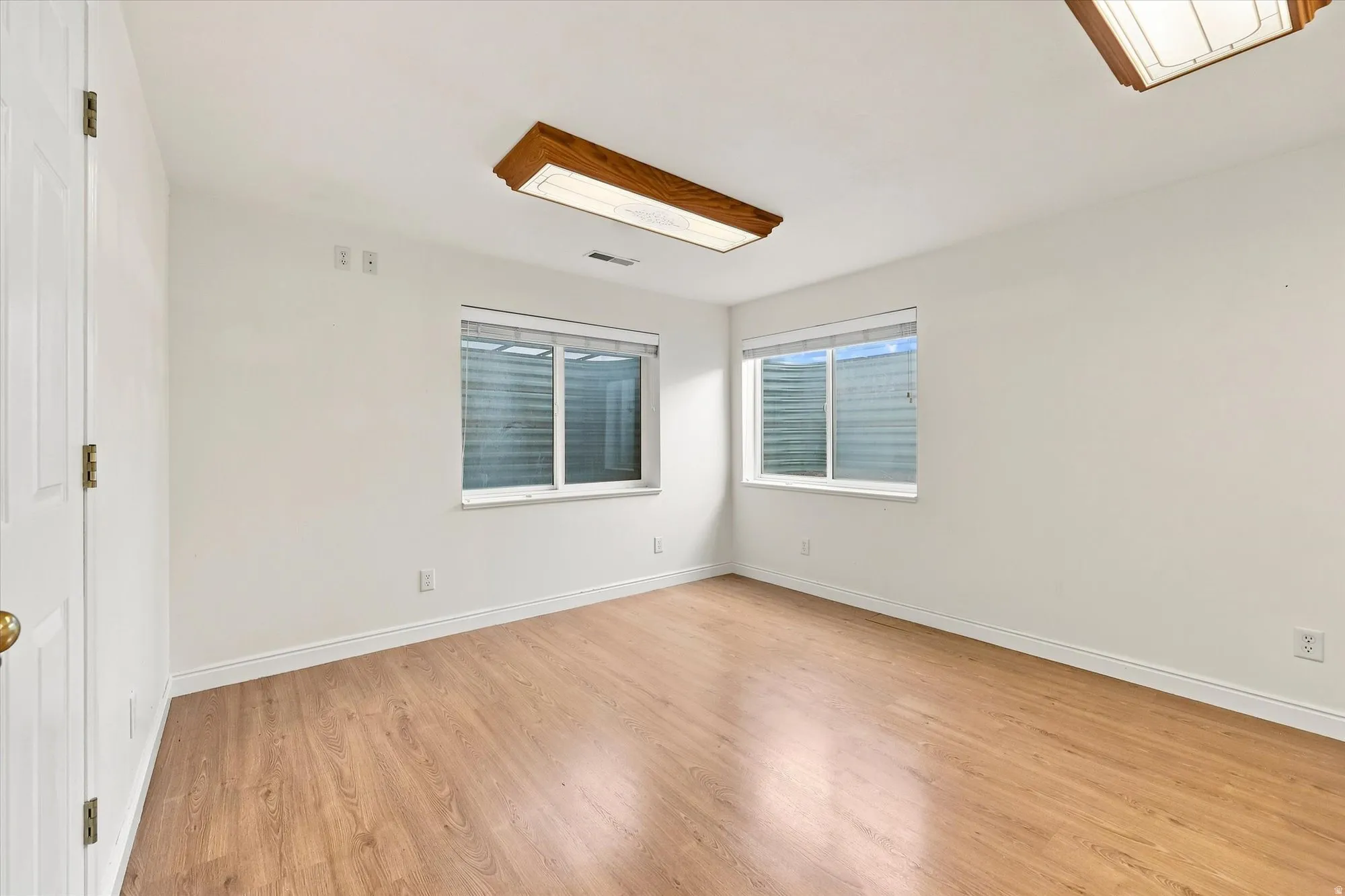 Wood-finish flooring, white walls, two windows with blinds, and recessed lighting
