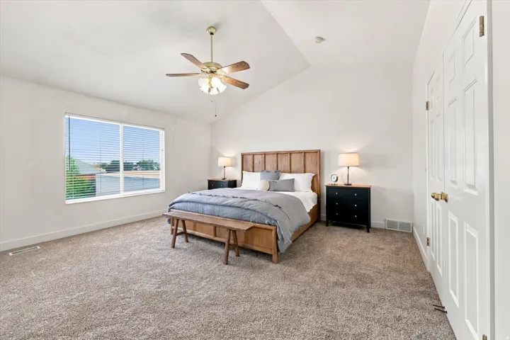 Vaulted ceiling with a ceiling fan, carpeted flooring, large window with blinds, and paneled doors