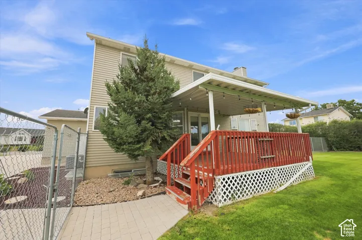 Rear exterior featuring a covered deck with red railings, light beige siding, and a chain-link fenced area