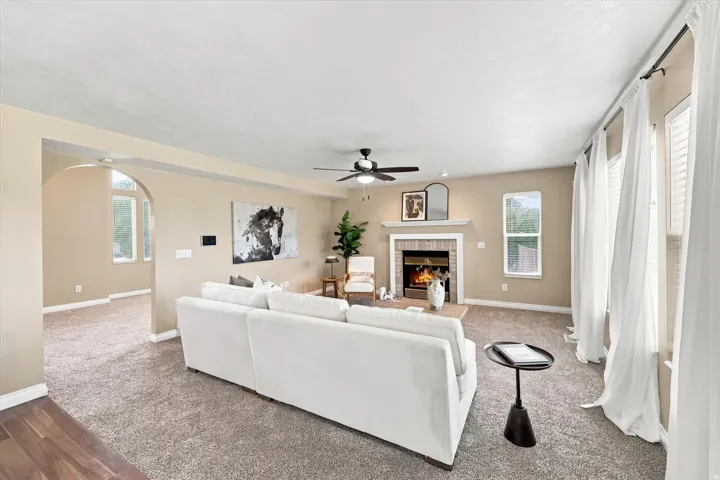 Spacious living area featuring a central fireplace with brick surround and mantle, multiple windows with white blinds, and a ceiling fan
