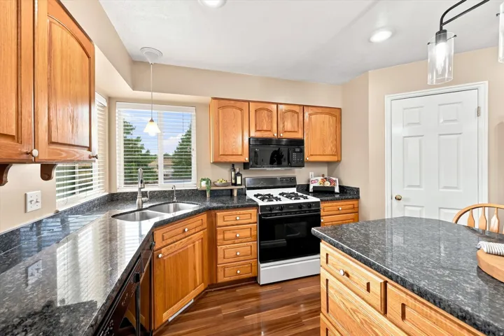 Kitchen featuring wood-finish cabinetry, dark speckled countertops, a double basin sink, and a built-in oven with a gas range