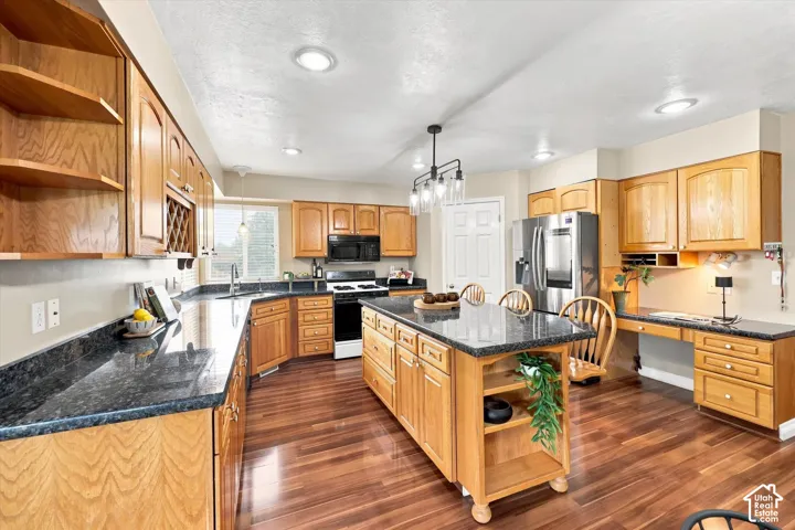 Spacious kitchen featuring wood-finish cabinetry, dark countertops, an island with seating, stainless steel appliances, and wood-finish flooring