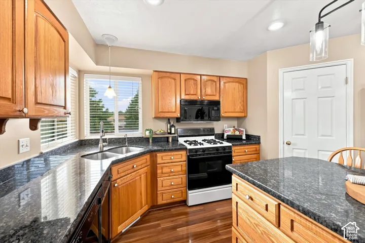 Kitchen featuring wood-finish cabinetry, dark speckled countertops, a double basin sink, and a built-in oven with a gas range