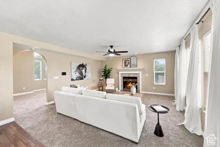 Spacious living area featuring a central fireplace with brick surround and mantle, multiple windows with white blinds, and a ceiling fan