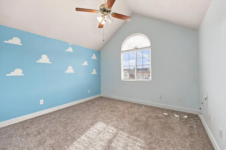 Vaulted ceiling with an attached ceiling fan, arched window with horizontal blinds, cloud-patterned accent wall, and carpeting