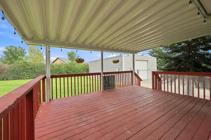Expansive covered deck with red-stained wood flooring and railing, offering an outdoor living space