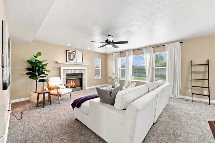 Open-concept living space featuring a fireplace with brick surround, ceiling fan, recessed lighting, and multiple windows