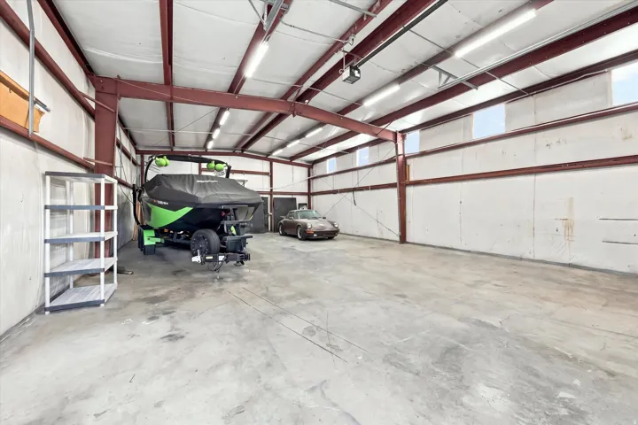 Expansive garage space featuring a concrete floor, exposed structural beams, ceiling-mounted lighting, and transom-style windows