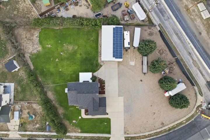 Spacious corner lot featuring a large outbuilding with rooftop solar panels, extensive gravel and grass areas, and a paved driveway