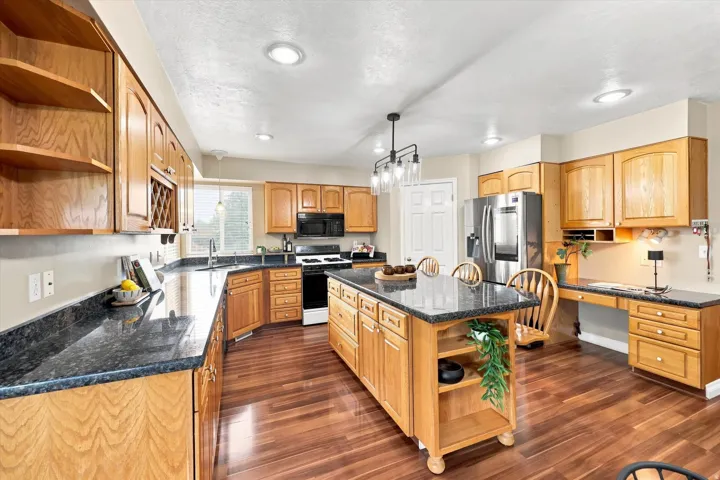 Spacious kitchen featuring wood-finish cabinetry, dark countertops, an island with seating, stainless steel appliances, and wood-finish flooring