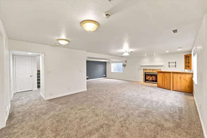 Expansive carpeted area featuring a built-in wet bar, a fireplace with a tile surround and mantel, and recessed lighting