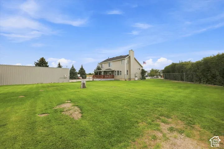 Expansive grassy lawn with a light-colored exterior dwelling, a detached metal-sided structure, and a wood deck