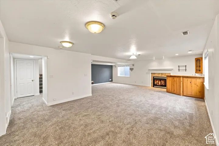 Expansive carpeted area featuring a built-in wet bar, a fireplace with a tile surround and mantel, and recessed lighting