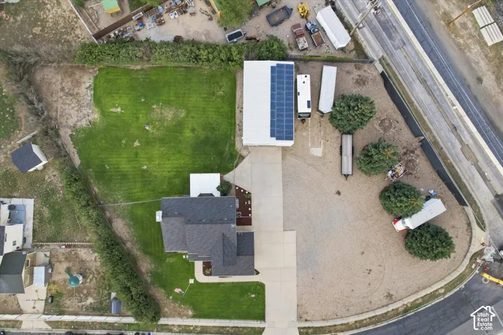 Spacious corner lot featuring a large outbuilding with rooftop solar panels, extensive gravel and grass areas, and a paved driveway