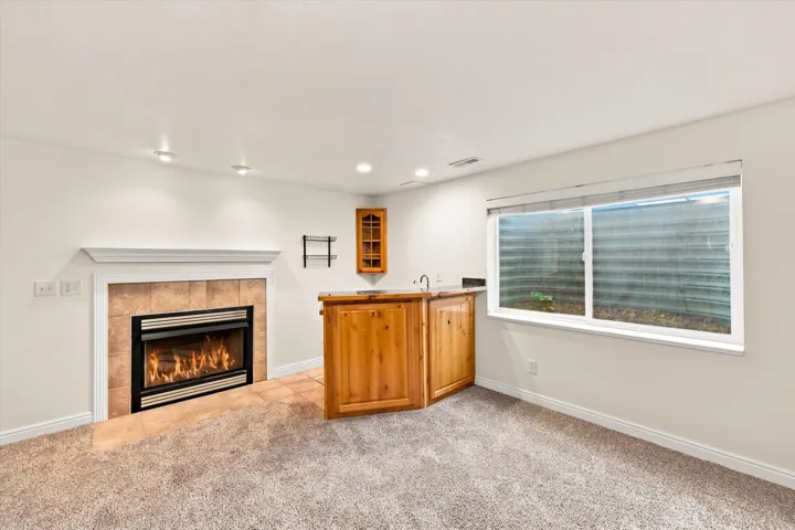 Recessed lighting, a fireplace with a tile surround and white mantel, and a built-in wet bar featuring wood cabinetry and a sink