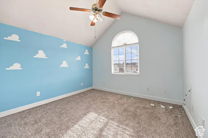 Vaulted ceiling with an attached ceiling fan, arched window with horizontal blinds, cloud-patterned accent wall, and carpeting