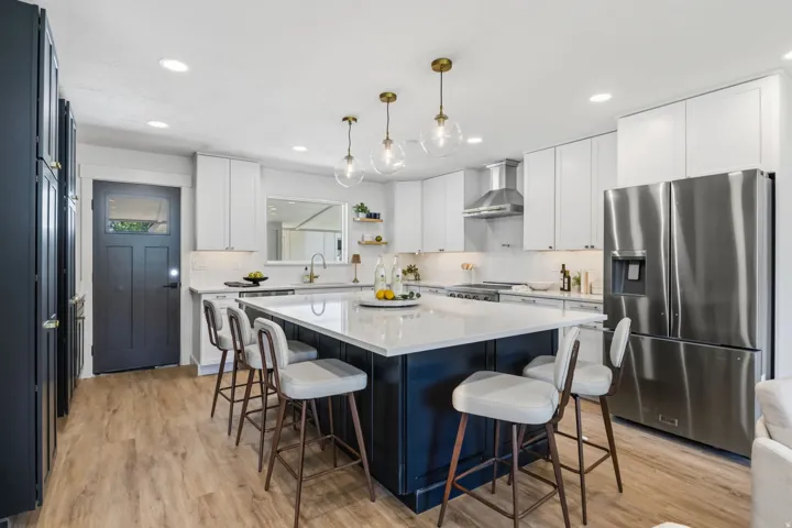 Spacious kitchen featuring an expansive center island, quartz countertop,stainless steel appliances, white upper cabinetry, a dark lower island, and wood-finish flooring