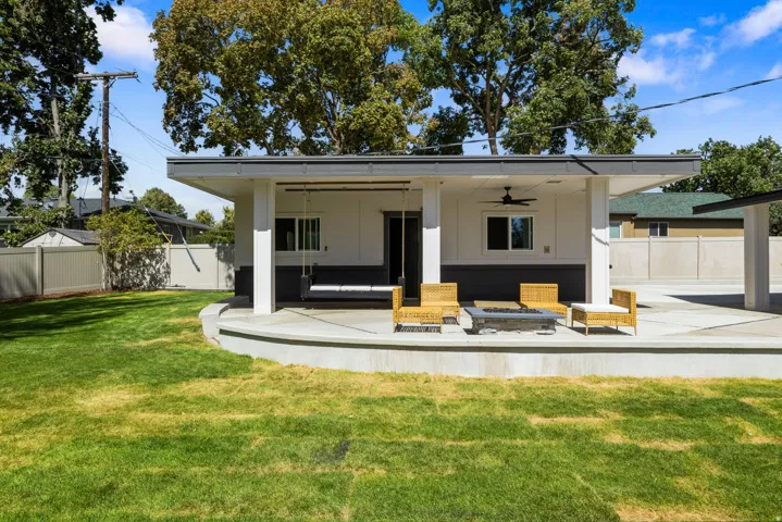 Expansive concrete patio with an integrated fire pit, covered outdoor living area, ceiling fan, and sliding glass door access