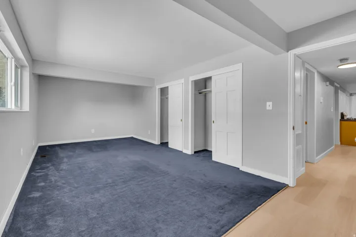 Blue carpeted flooring, light grey wall paint, multiple built-in closets with bi-fold doors, and a window providing natural light