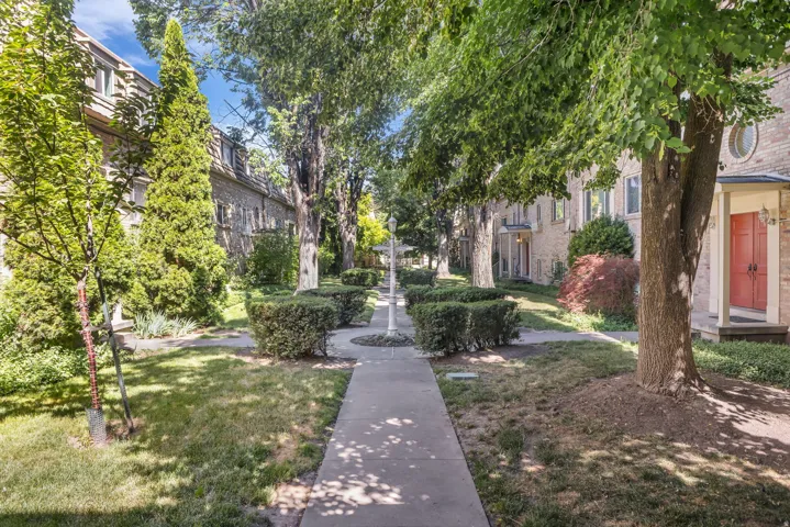 Sidewalk entry with mature trees, established landscaping, and traditional brick facade