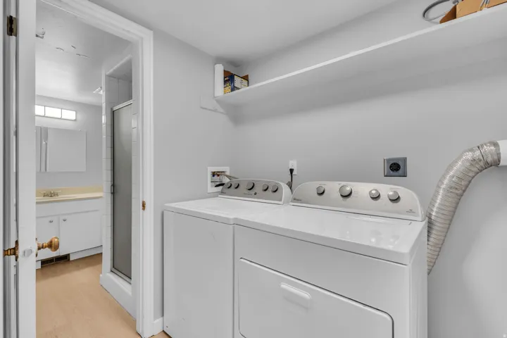 Built-in laundry appliances, overhead shelving, light wood-finish flooring, white vanity with integrated sink, and a glass-enclosed shower