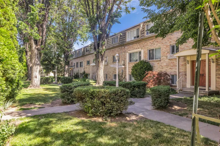 Brick exterior with multiple windows and dormers, featuring mature landscaping with manicured shrubs and established trees