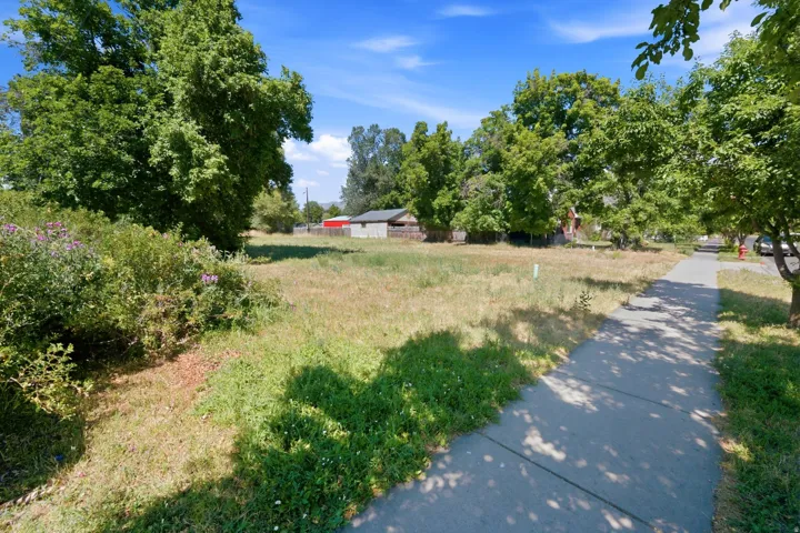 Expansive land parcel featuring existing trees, a paved sidewalk, and open space