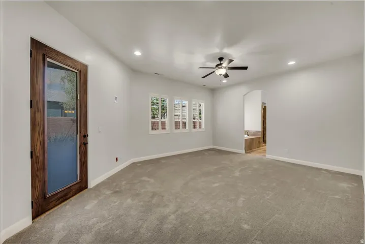 Spacious carpeted room featuring a ceiling fan with integrated lighting, recessed ceiling lights, and multiple windows with plantation shutters
