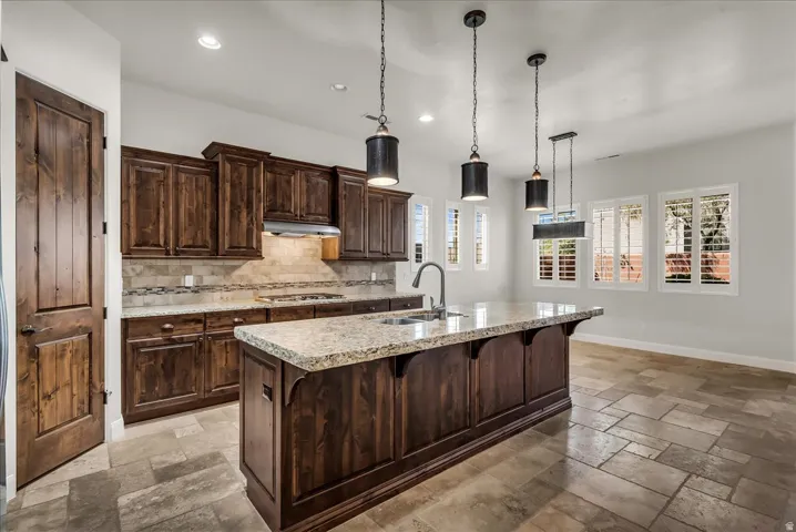 Gourmet kitchen featuring rich wood cabinetry, stone countertops, a large center island with an undermount sink, and recessed lighting